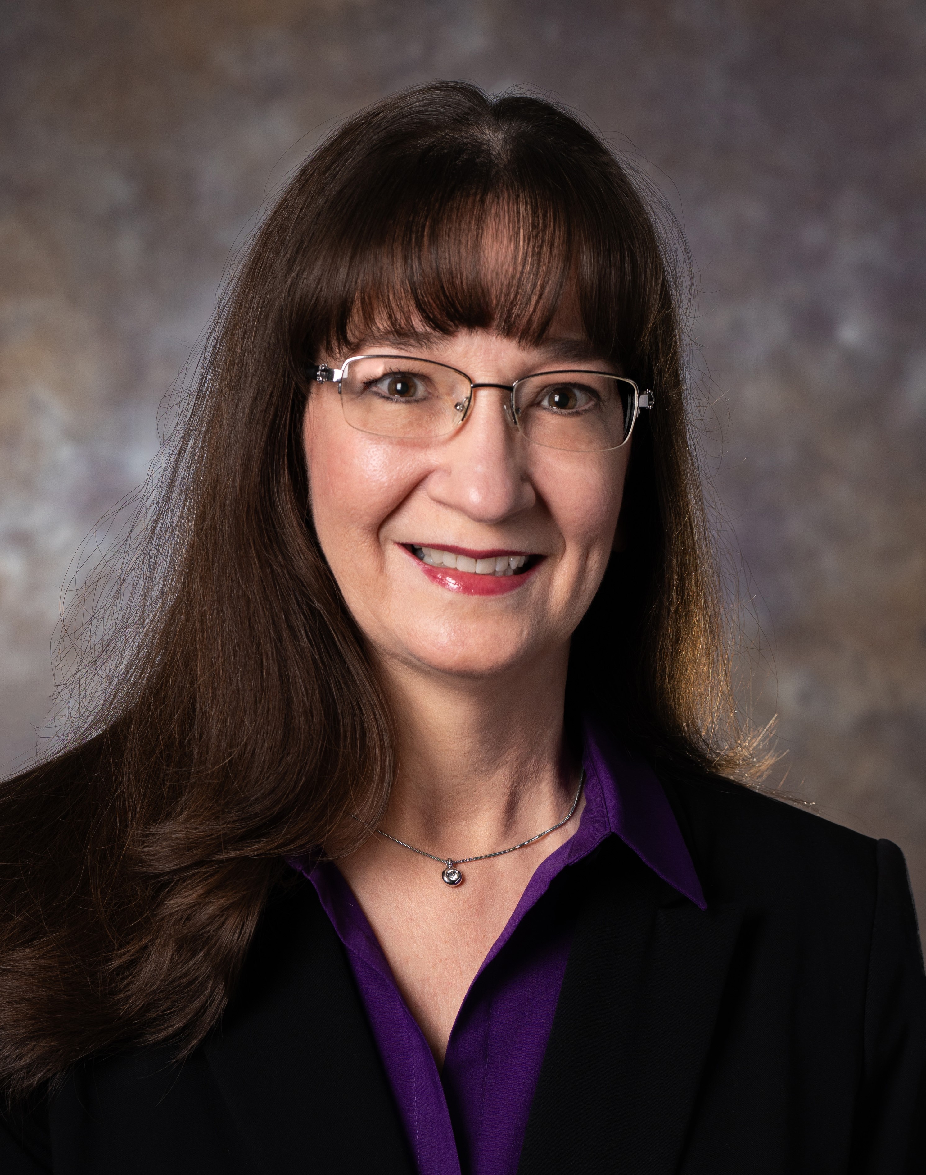 Woman with long dark hair and glasses smiling at the camera