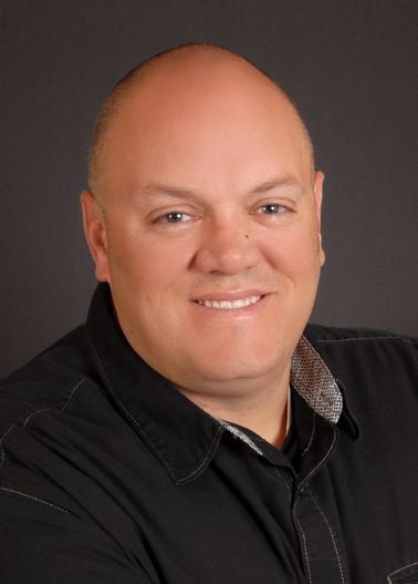 Portrait of Bob Lamoreaux bald man wearing black button down shirt smiling at camera