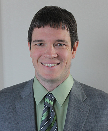 Portrait of Caleb Stock - a man with a gray suit and green tie smiles at the camera