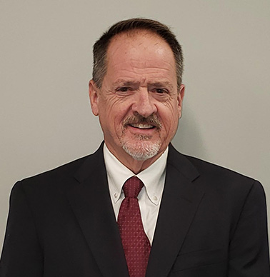 Portrait of Christopher Humphreys - a man wearing a suit with a red tie smiles at the camera