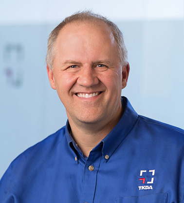 Portrait of Craig Bursch - a man wearing a blue shirt smiles at the camera