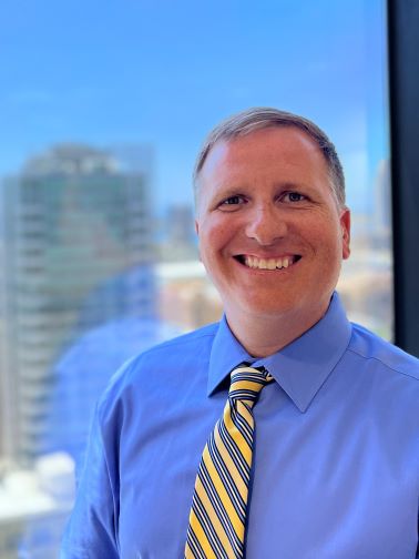 Portrait of Craig Shannon - Man in blue shirt and striped tie smiling at camera