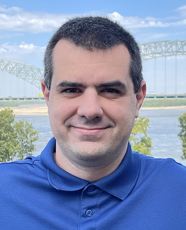 Portrait of Evan Boulanger - a man wearing a blue shirt smiles at the camera