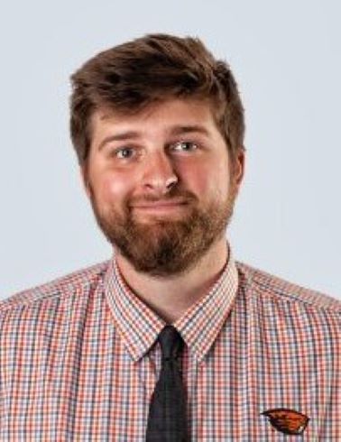 Portrait of Jamestaun Kraupp - bearded man in plaid shirt and tie smiling at camera