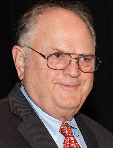 Portrait of John Rogers - a man wearing a suit smiling at the camera