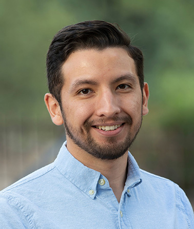 Portrait of Jose Aguilar. Photo of a brown haired man wearing a pale blue shirt smiling at the camera.