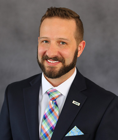 portrait of Kensey Russell. A brown haired man wearing a suit and tie smiling at the camera.