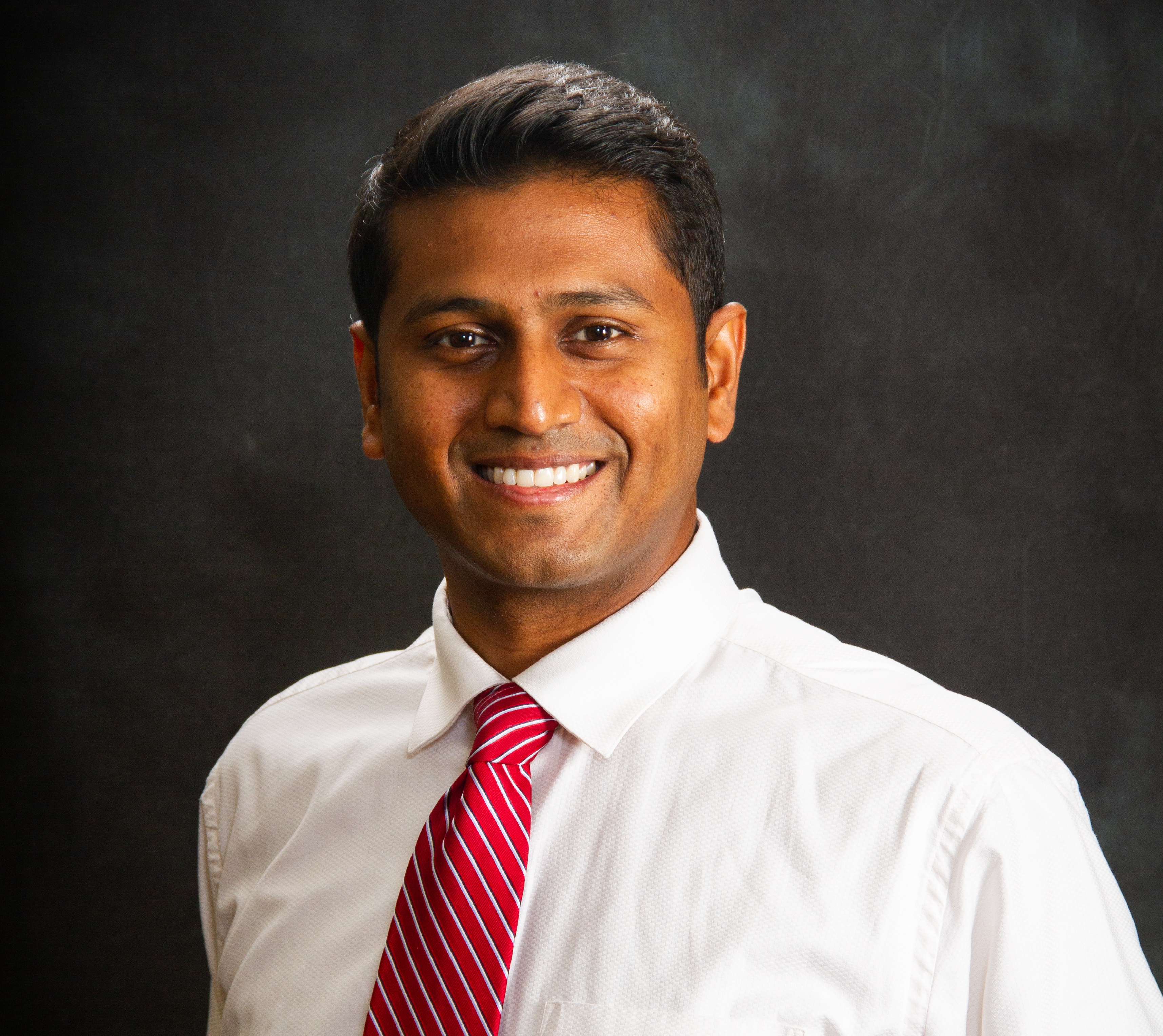 Man in white shirt and red tie smiling at camera