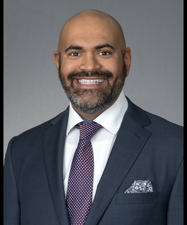 Portrait of Patrick Kaimrajh - a blad man wearing a grey suit smiles at the camera