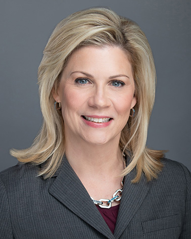Portrait of Susan K. Roth - a woman with blonde hair wearing a gray suit smiles at the camera