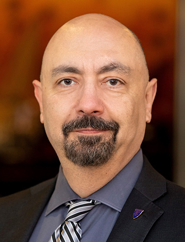 Portrait of Yazdan Emrani - a man with a goatee wearing a suit smiles at the camera