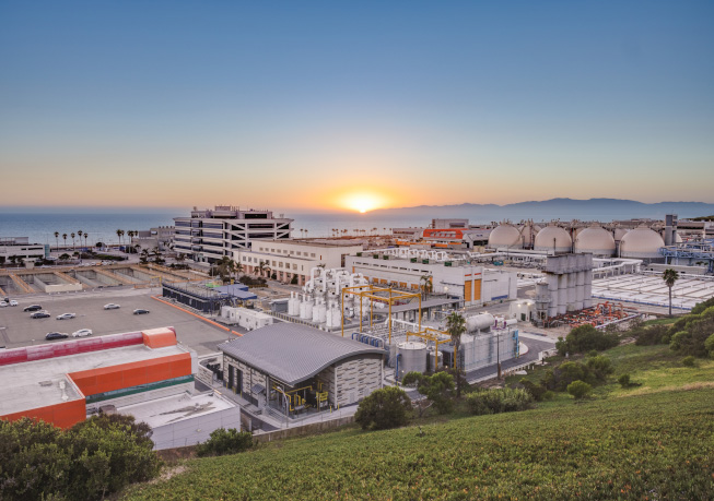 Wide view of the Hyperion Water Purification Facility at sunset, showing processing buildings and coastal surroundings.