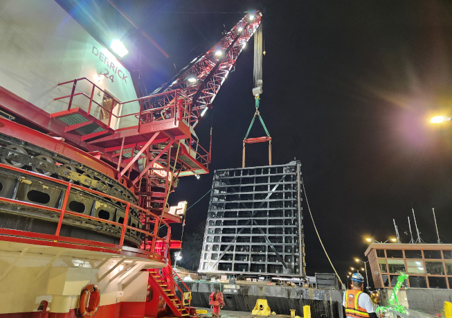 Nighttime construction view of the Lake Washington Ship Canal large lock miter gate replacement, with cranes lifting a massive steel gate.