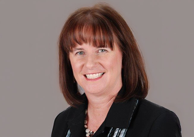 Studio headshot of an adult professional wearing a dark blazer and patterned top, photographed against a light neutral background.