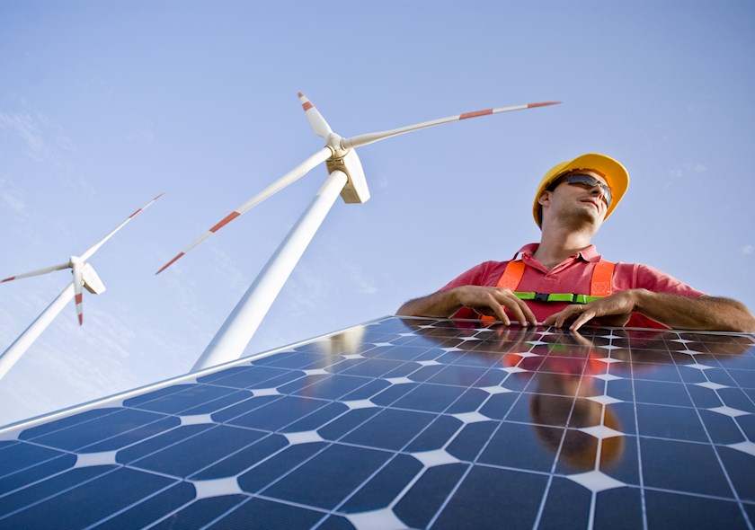 An engineer leaning on a solar panel with two windmills in the background.