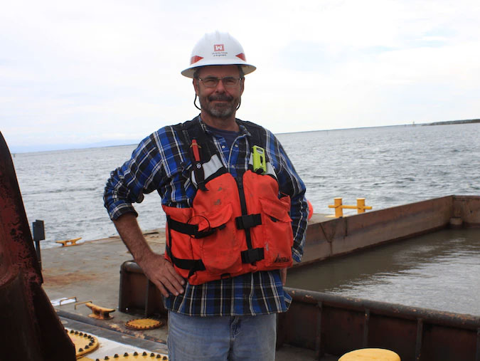 Photo of Tim Welp wearing a utility vest on a dock.