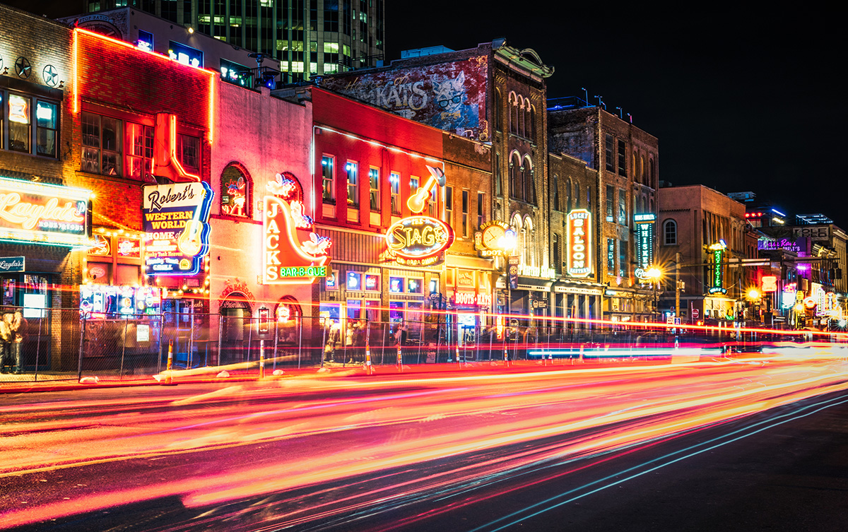 Lights trails from traffic at night on Lower Broadway, in the heart of Nashville's historic music district, with a long series of neon signs advertising music bars along the street.