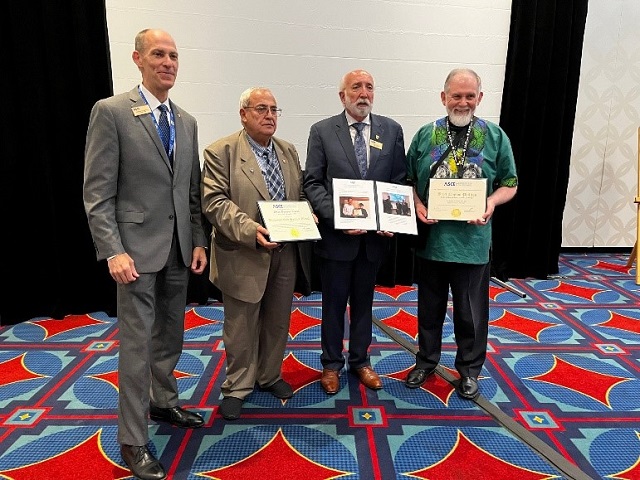 R10 DSM Award Ceremony at the Global Reception of the ASCE 2022 Convention. Pictured are 4 people standing in front of a screen, holding awards and smiling at the camera. 