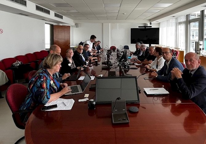 Pictured: Fifteen people sitting at a conference table having  a meeting