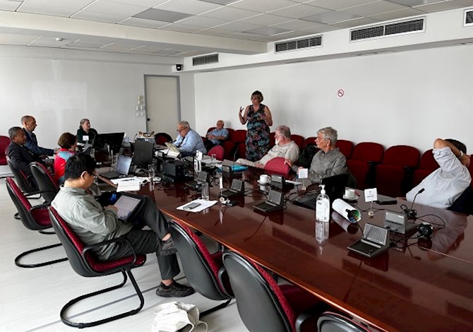 Pictured: Ten people sitting at a table and one person standing giving a presentation.