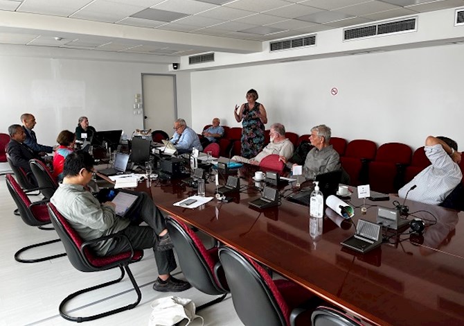 Pictured: Ten people sitting at a table and one person standing giving a presentation. 