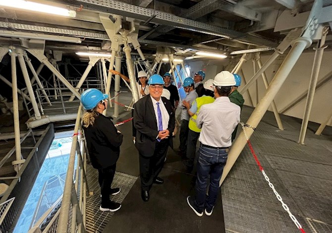 Pictured: Nine people with hard hats on at a construction site. One person is facing the camera and smiling.