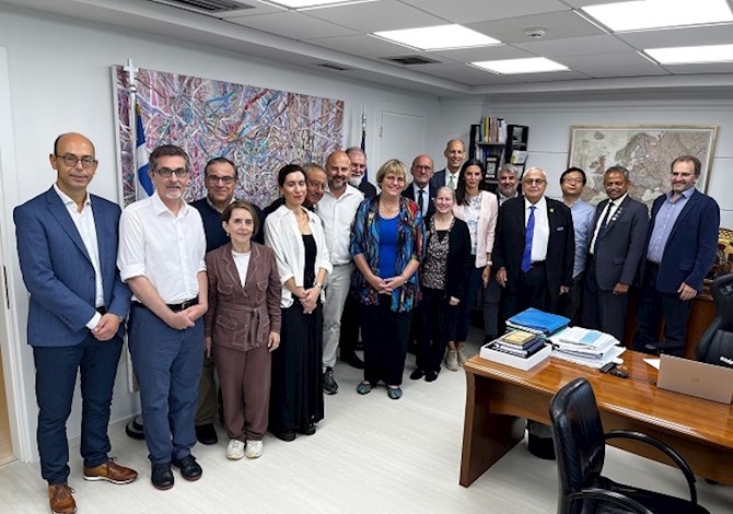 Pictured: Eighteen people standing in a room smiling at the camera. 