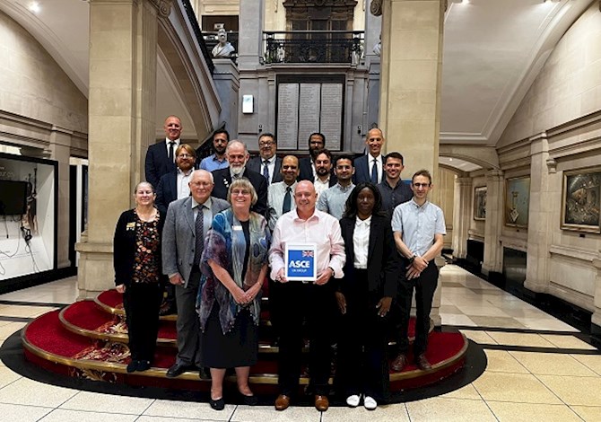 Pictured: Seventeen people standing on stairs in front of a plaque smiling at the camera