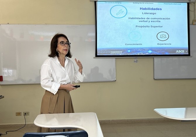 One person standing in the front of a classroom, to the left of a screen, giving a presentation