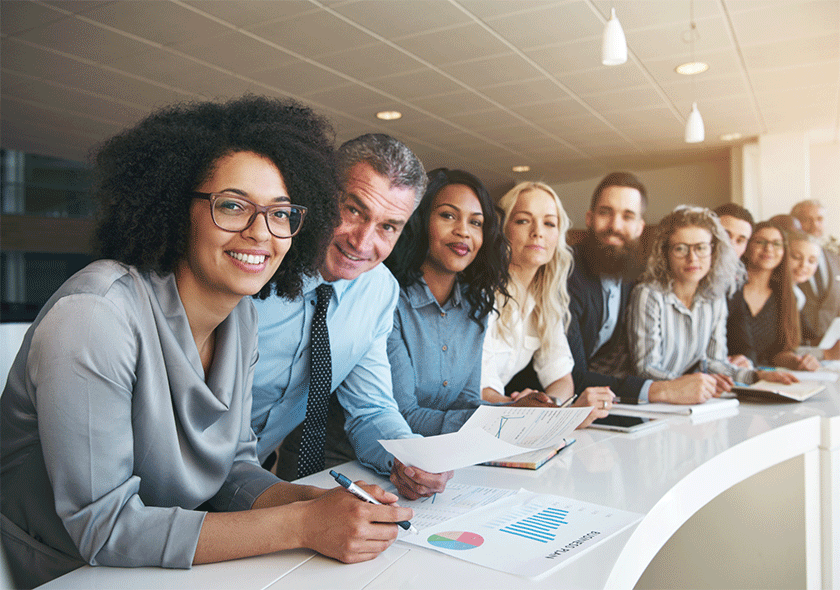 Group of diverse men and women at a table looking at you.