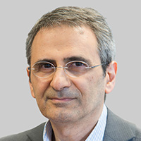 Man wearing wire-rimmed glasses looks at the camera. 