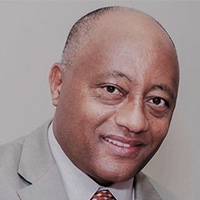 Man with brown skin in suit and tie smiles at the camera.