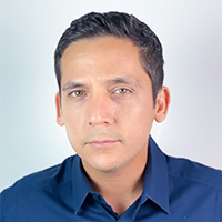 A man in a dark Oxford shirt smiles at the camera.