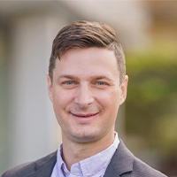 man in gray jacket and white shirt smiles at the camera
