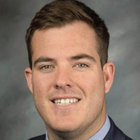 Man in jacket and tie smiles at the camera.