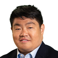 A man wearing a jacket and button-down shirt smiles at the camera. 