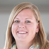 Woman with blonde hair with a scarf around her neck smiles the camera. 
