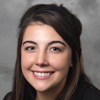 Woman with brown hair and eyes in a black suit smiles at the camera. 