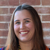 A woman with brown hair wearing a colorful top smiles at the camera. 