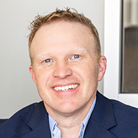 A man wearing a white shirt and black jacket smiles at the camera. 