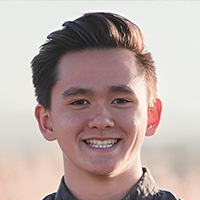 Young man in gray button-down shirt smiles at the camera.  