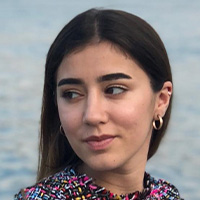 A woman with long dark hair in a patterned top looks off to the left. 