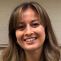 A woman with long brown hair, wearing a sleeveless dark top, smiles at the camera. 