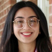 A woman with glasses and thick brown hair smiles at the camera. 
