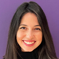 A woman with long dark hair, wearing a dark turtleneck, smiles at the camera. 