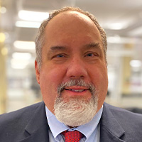 Man with gray goatee and close cropped hair smiles at the camera. 