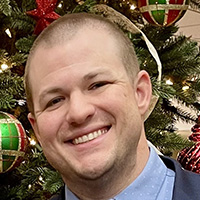Man in blue shirt and jacket smiles at the camera.