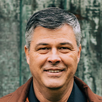 man in brown suede jacket smiles at camera