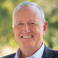 Man in shirt and jacket smiles at the camera.