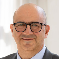 Bald man with glasses wears jacket and tie and smiles at the camera. 